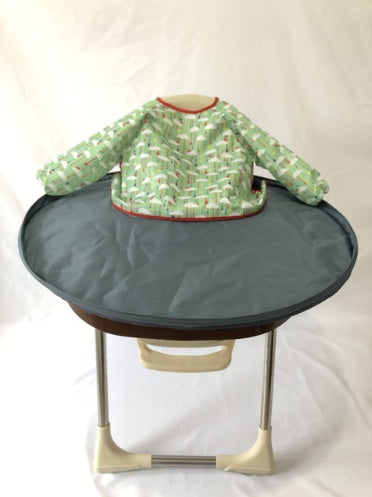 Green patterned baby bib on a round gray tray with a white background