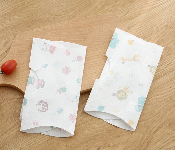 Two packs of patterned paper towels on a wooden surface with a cherry tomato.