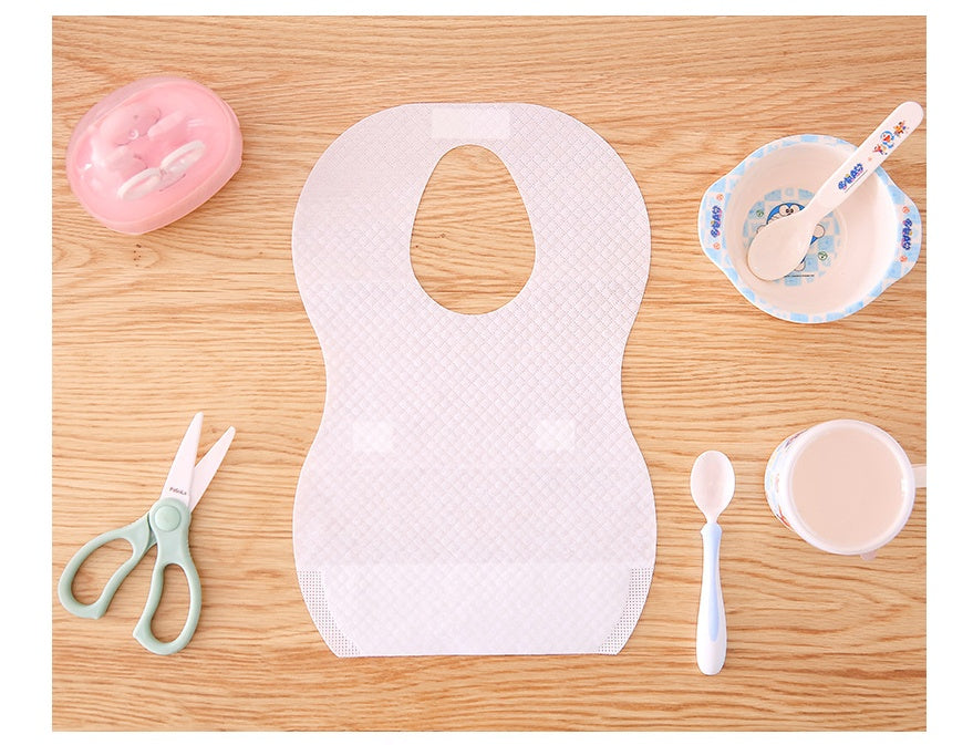 White bib on a wooden surface with baby-related items like spoons and bowls.