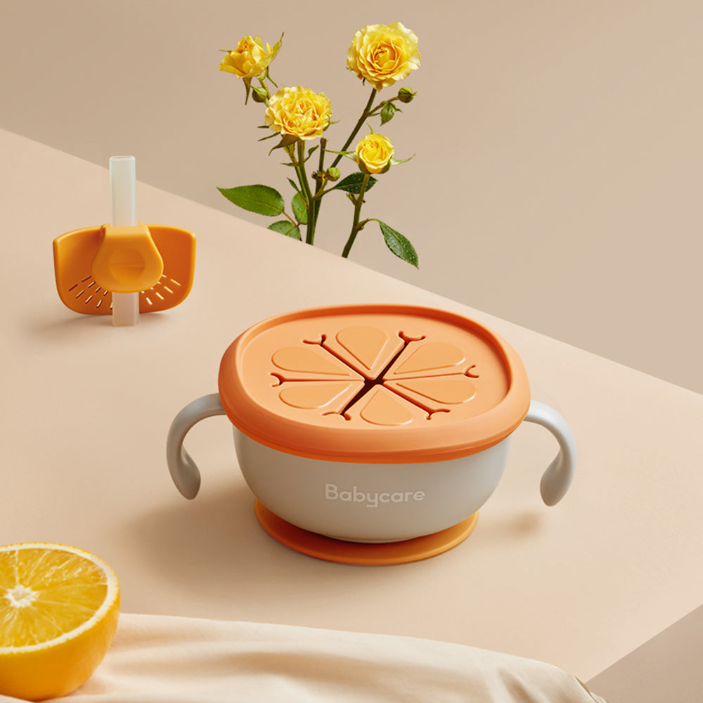 Baby cup with orange lid and handles, surrounded by yellow flowers and an orange fruit on a beige background.
