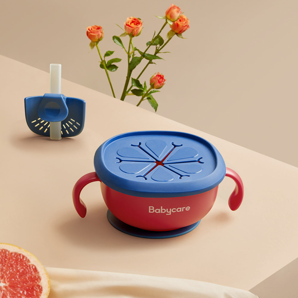 Red and blue baby cup with a lid on a beige surface with flowers and a fruit slice.