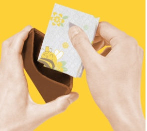 Hands holding a small brown wallet with a card featuring cartoon characters on a yellow background