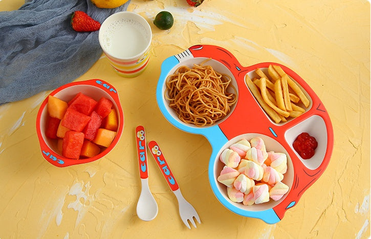 Colorful children's plate with compartments filled with food, accompanied by a fork and spoon on a yellow surface.