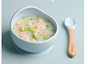White bowl with a baby food puree and a wooden spoon on a light blue background