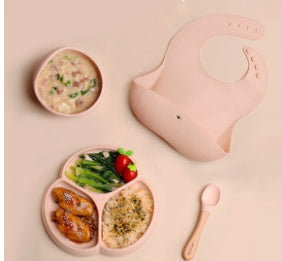 Children's meal set with divided plate, bowl, and bib on a pink background