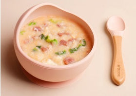 Pink bowl of soup with a wooden spoon on a light pink background