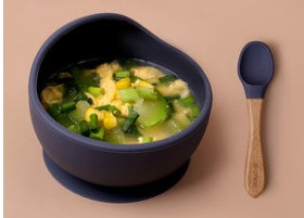 Soup bowl with green vegetable soup and a wooden spoon on a beige background