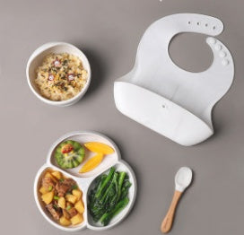 Children's plate with compartments, bowl, bib, and spoon on a gray background