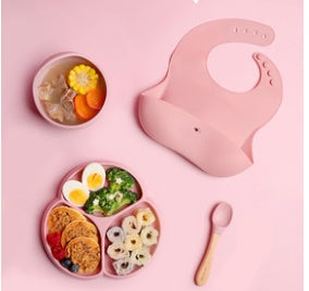 Children's meal set with pink plate, bib, and spoon on a pink background