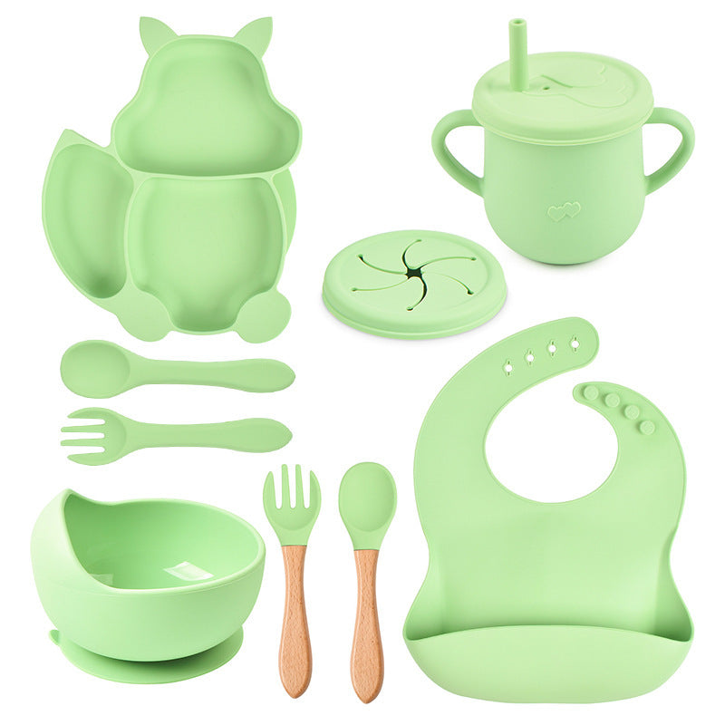 Green silicone baby utensil set including bowl, spoon, fork, cup, and bib on a white background