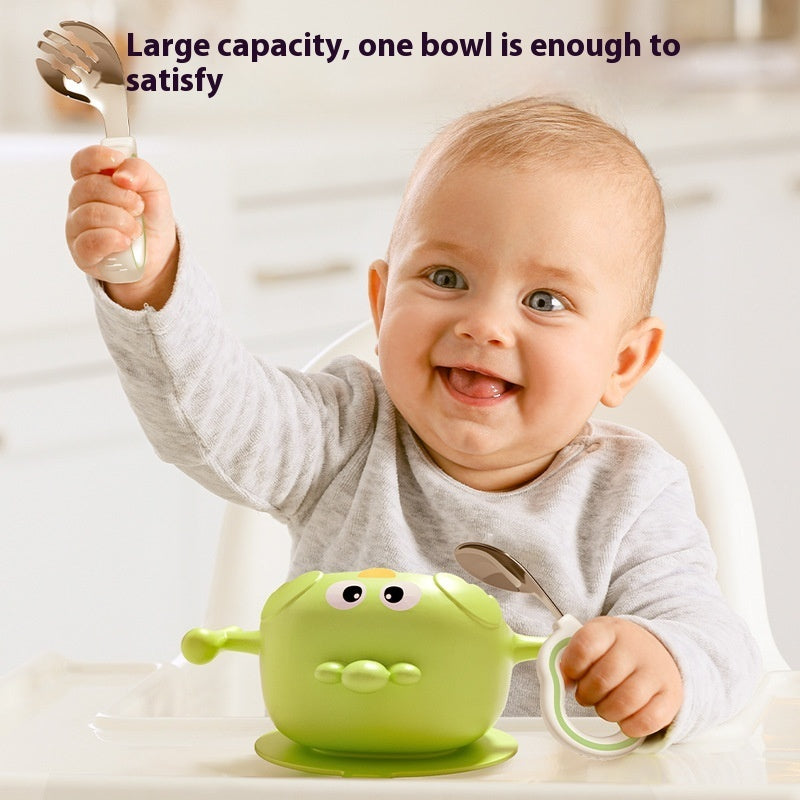 Baby holding a green bowl with a spoon and fork, smiling.