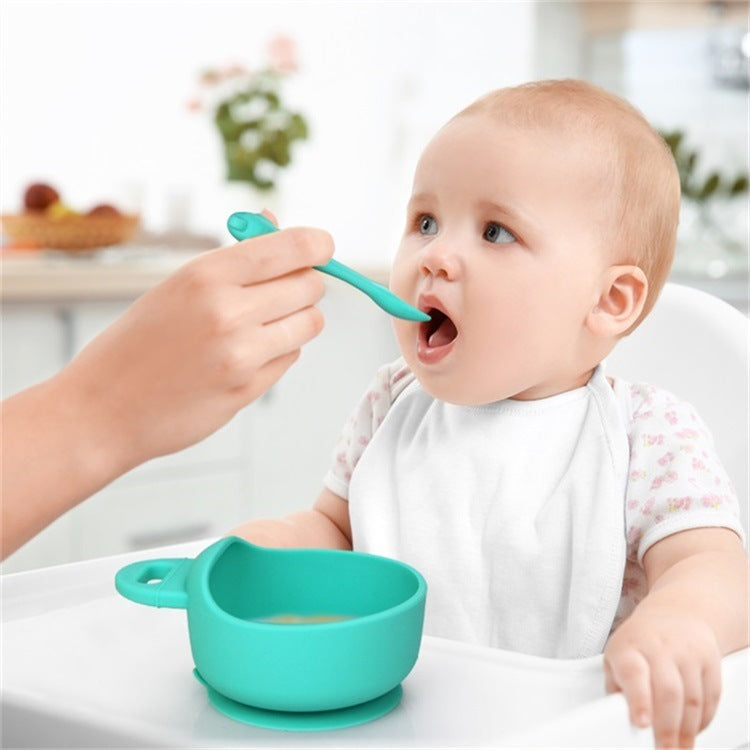Baby being fed with a green spoon and bowl in a home setting