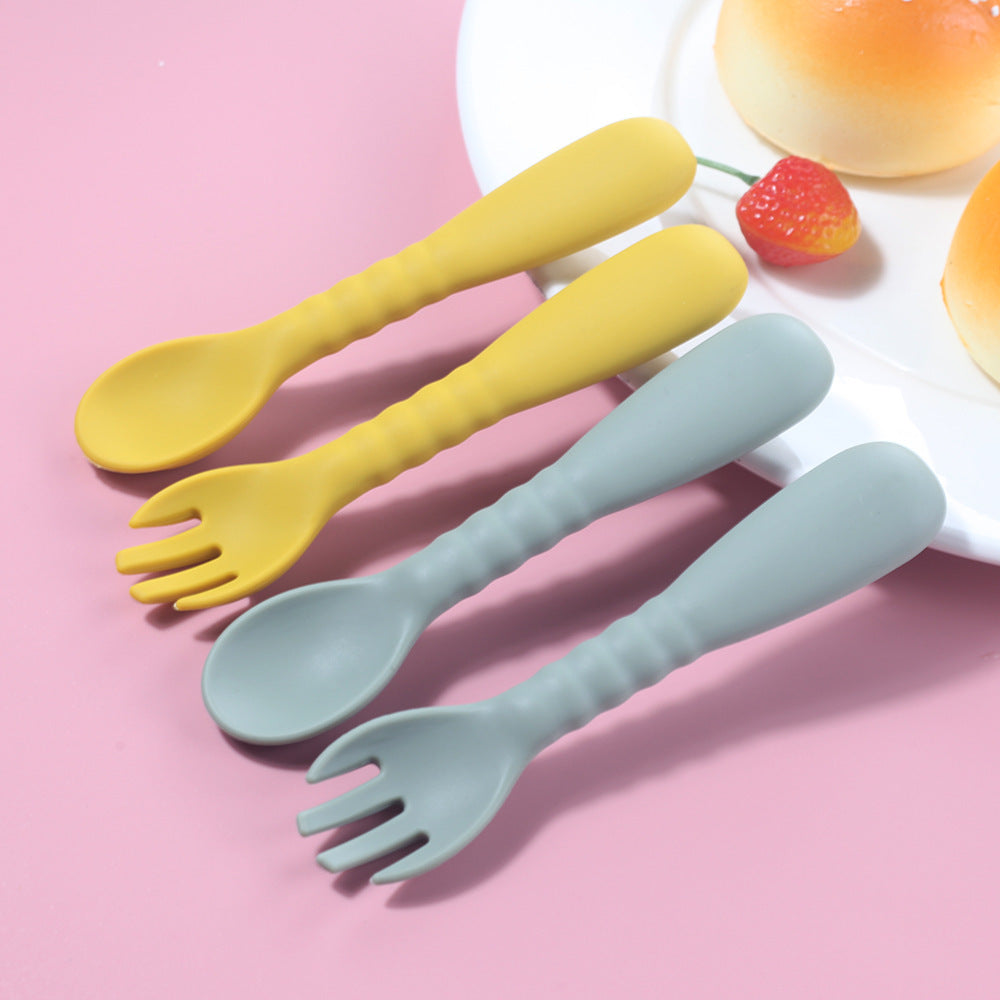 Set of yellow and light blue plastic spoons and forks on a pink background with a plate of food.