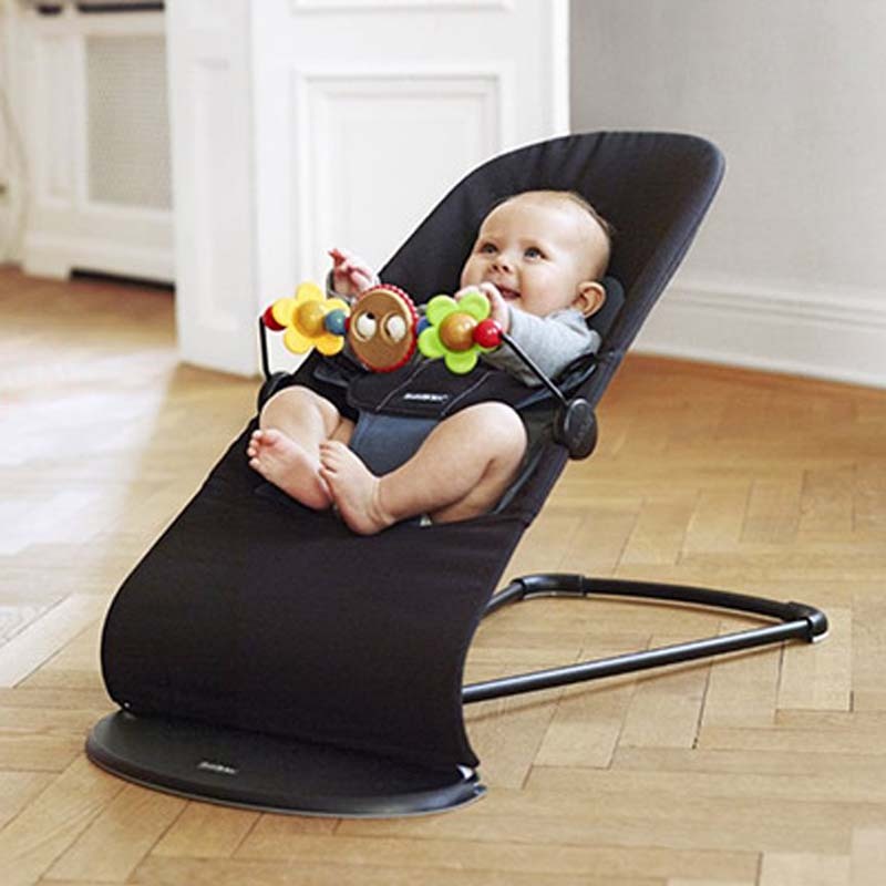 Baby in a black baby bouncer with colorful toys on a wooden floor.