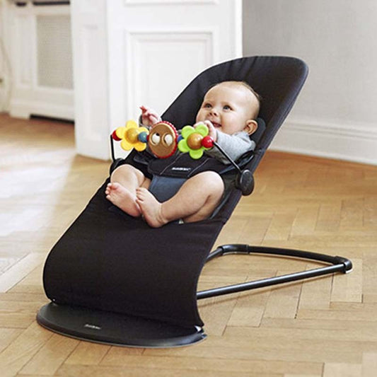 Baby in a black baby bouncer with colorful toys on a wooden floor.
