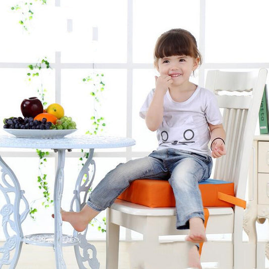 Child sitting on a chair with an orange cushion, smiling, in a bright room with a table and fruits.