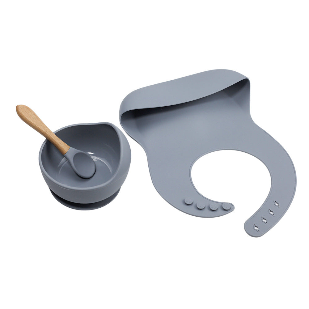 Gray silicone bib, bowl with spoon, and wooden spoon on a white background