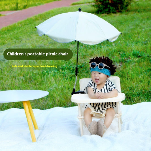 Child sitting in a portable picnic chair with an umbrella in a grassy outdoor setting