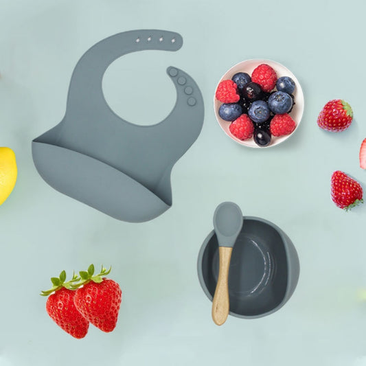 Gray silicone bib, bowl, and spoon with berries on a light blue background