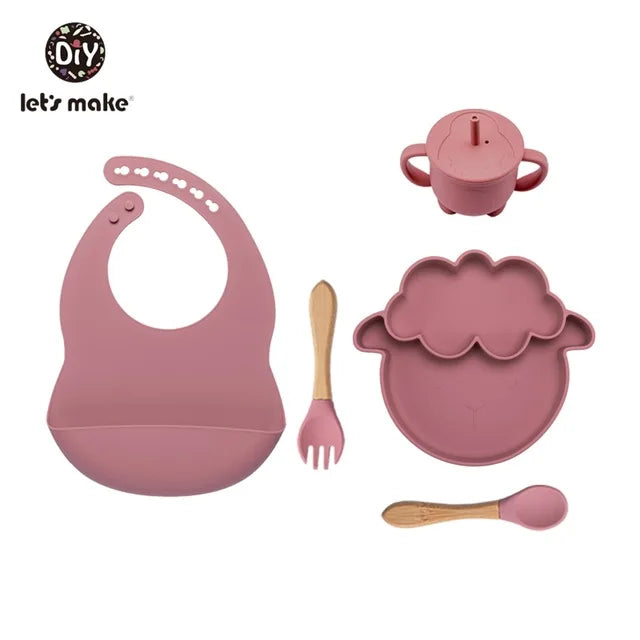 Pink baby dining set with bib, plate, cup, and utensils on a white background.