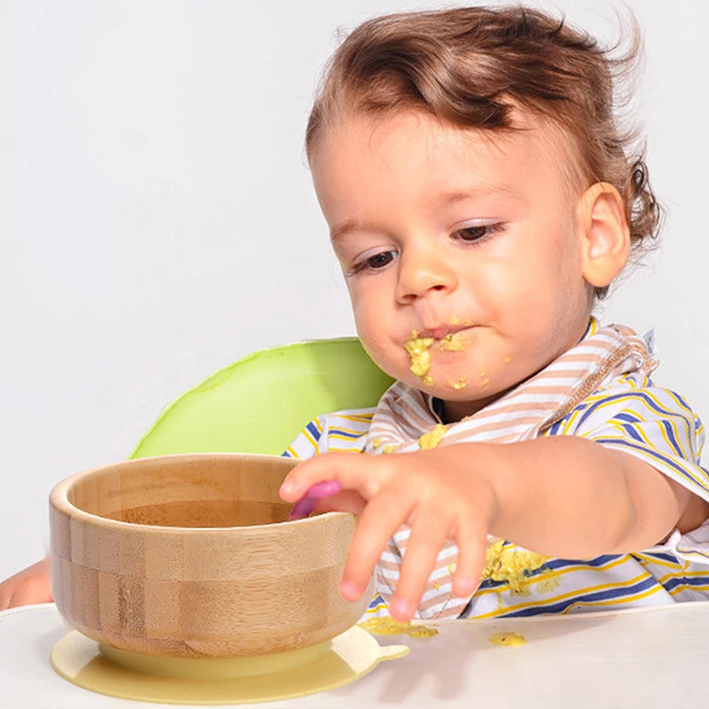 Child in a high chair with a wooden bowl and a bib, on a plain background