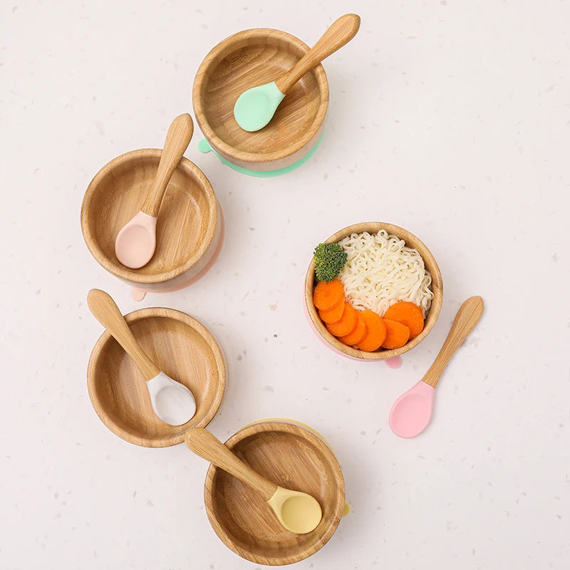 Set of wooden bowls and spoons on a light surface with food items.
