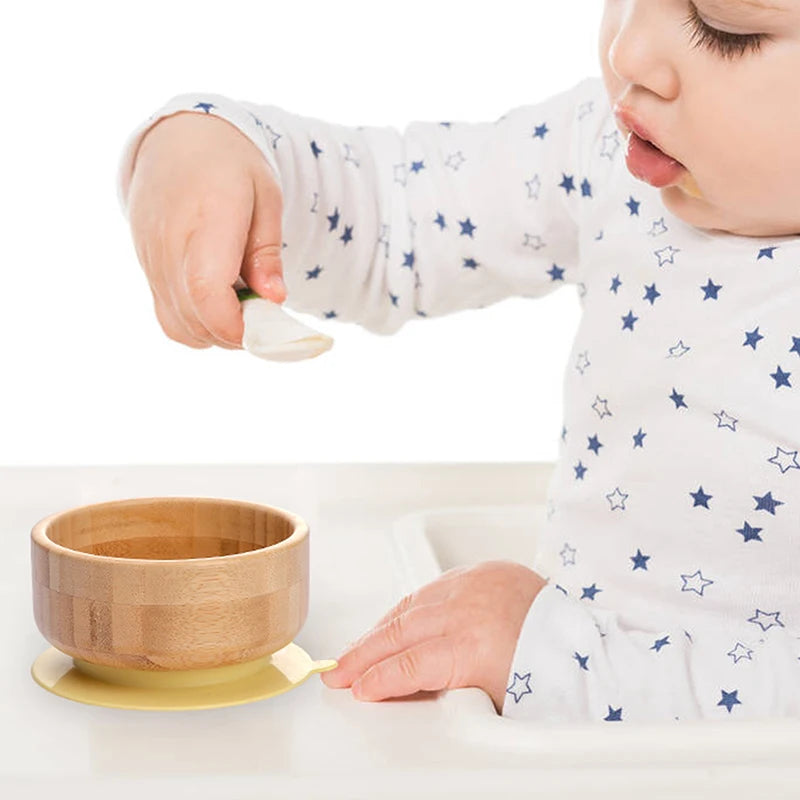 Baby in a white onesie with star patterns using a wooden bowl and spoon on a white background