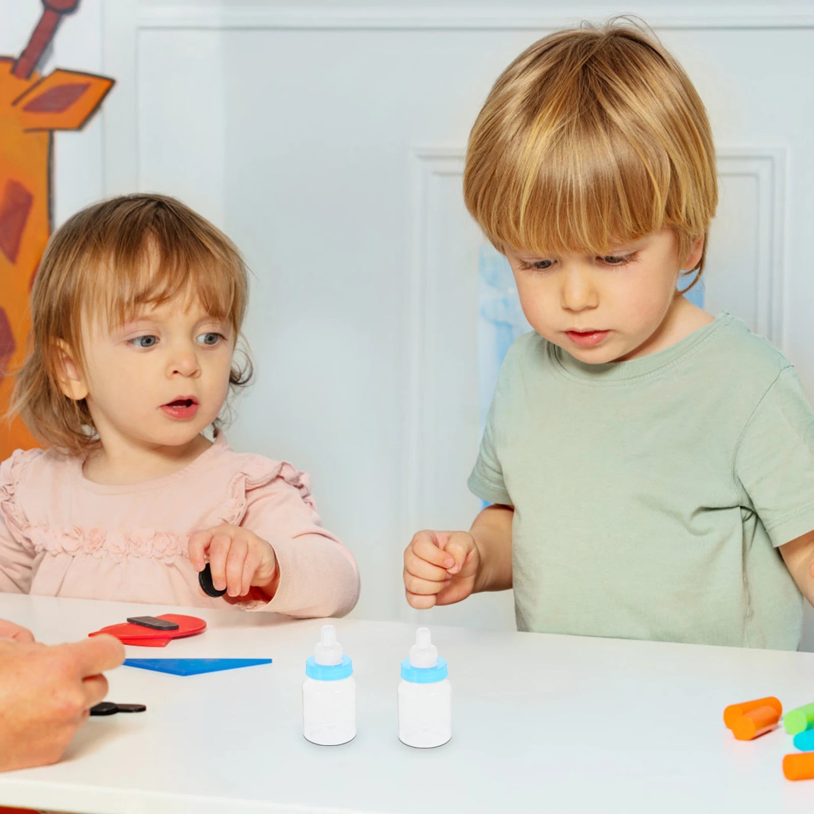 Two children sitting at a table with bottles and toys, engaged in an activity.