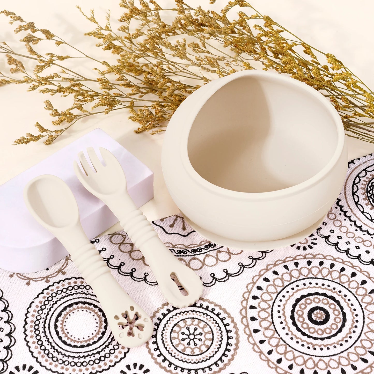 Ceramic cup with spoon and fork on a decorative tablecloth with gold flowers.