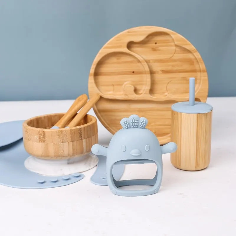Set of wooden and silicone baby utensils on a white surface with a blue background