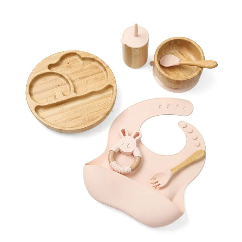 Children's wooden dining set with plate, cup, spoon, and bib on a white background