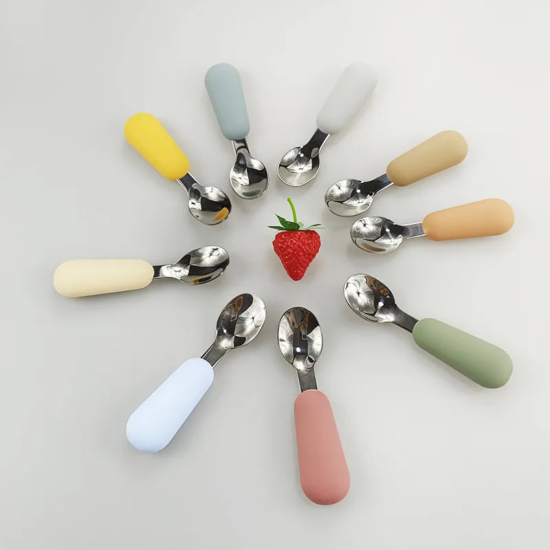 Set of colorful spoons with silicone handles arranged around a strawberry on a light gray background