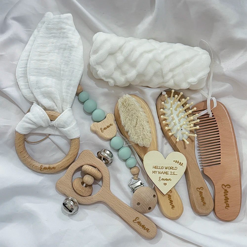 Collection of baby care items including a teether, rattle, and brushes on a white fabric background.