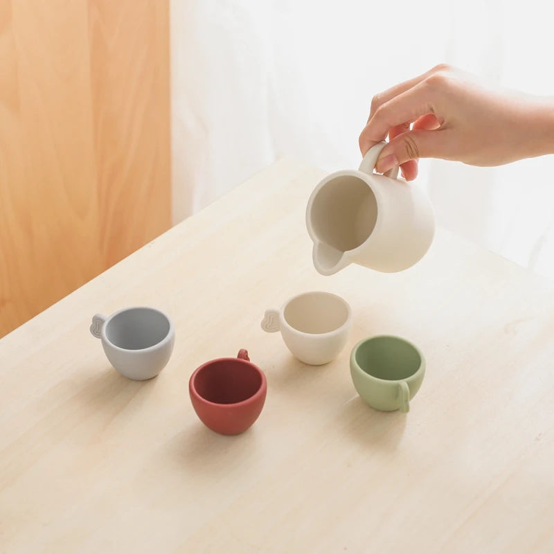 Hand pouring from a white mug into a small red cup on a light surface.