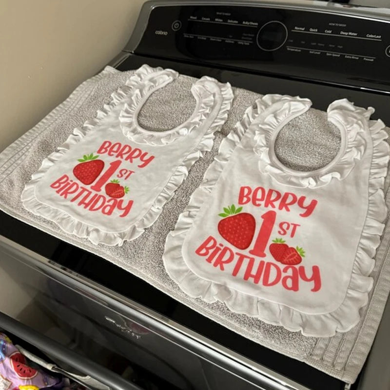 Two bibs with 'Berry 1st Birthday' text on a stovetop.