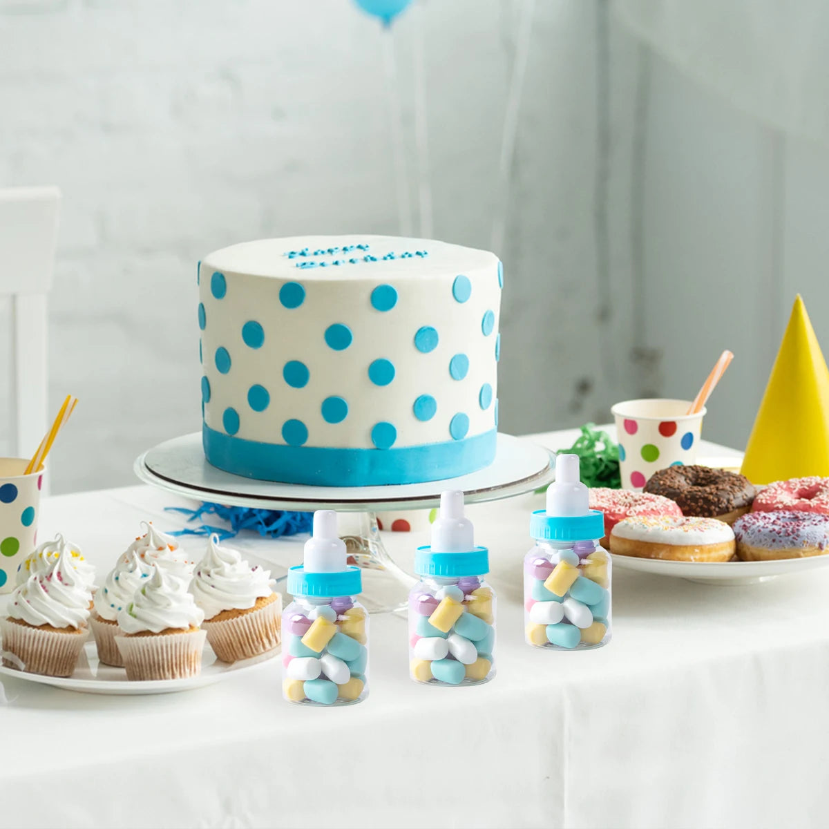 Polka dot birthday cake with cupcakes, donuts, and candy bottles on a table.