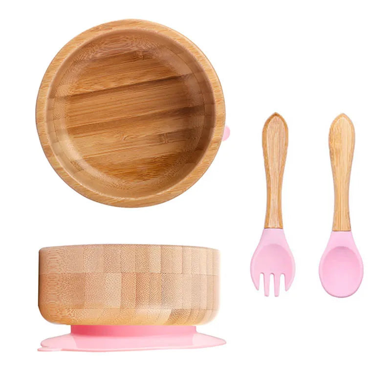 Bamboo bowl with pink silicone base and matching fork and spoon on a white background