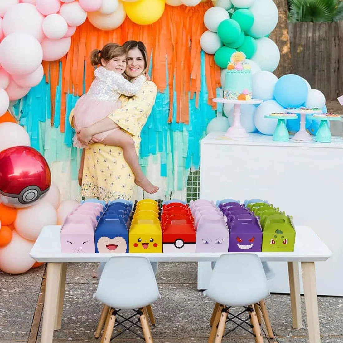 Woman holding a child in front of a colorful balloon arch with a table featuring cartoon-themed cups.