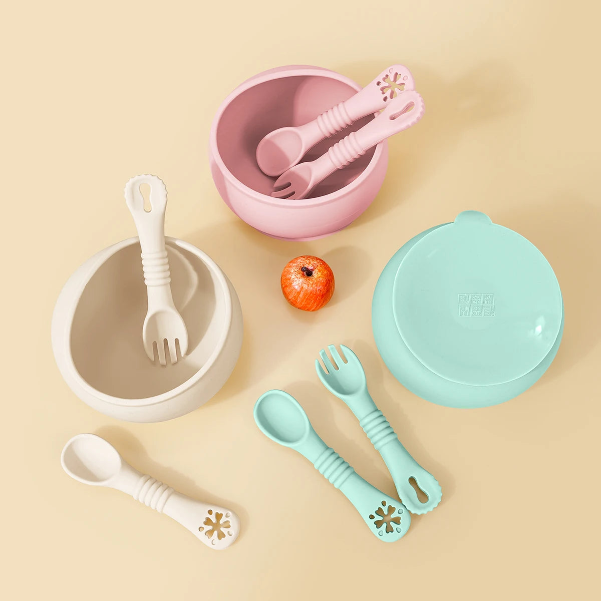 Set of colorful children's tableware including bowls, spoons, and forks on a beige background.