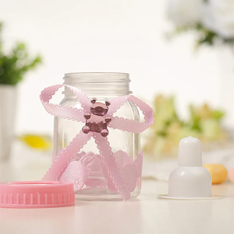 Pink baby teether with a lace bow in a glass jar on a white surface.