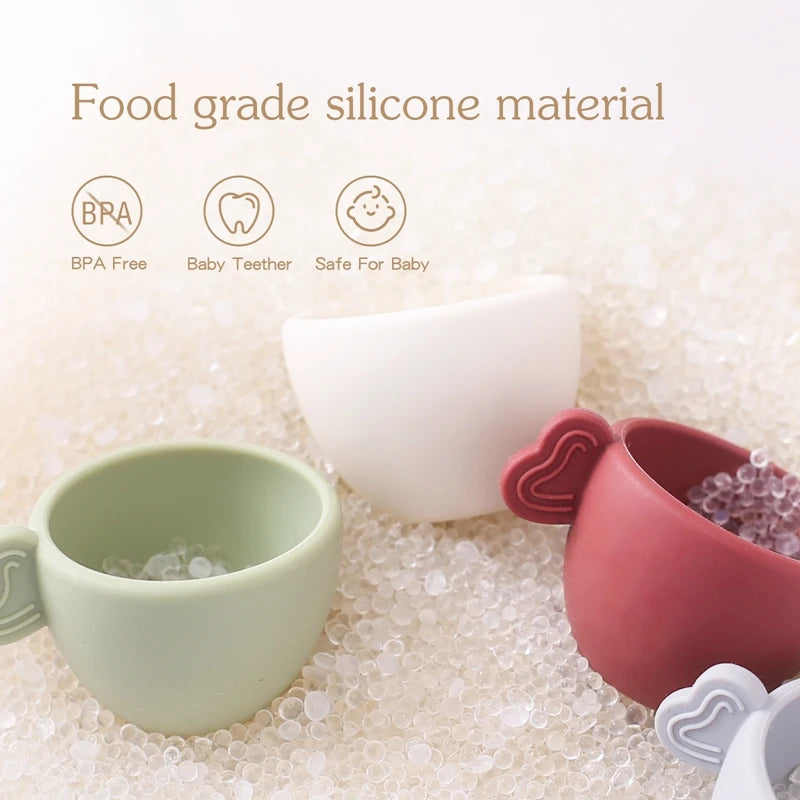 Silicone baby cups with food-grade material certification on a textured surface.