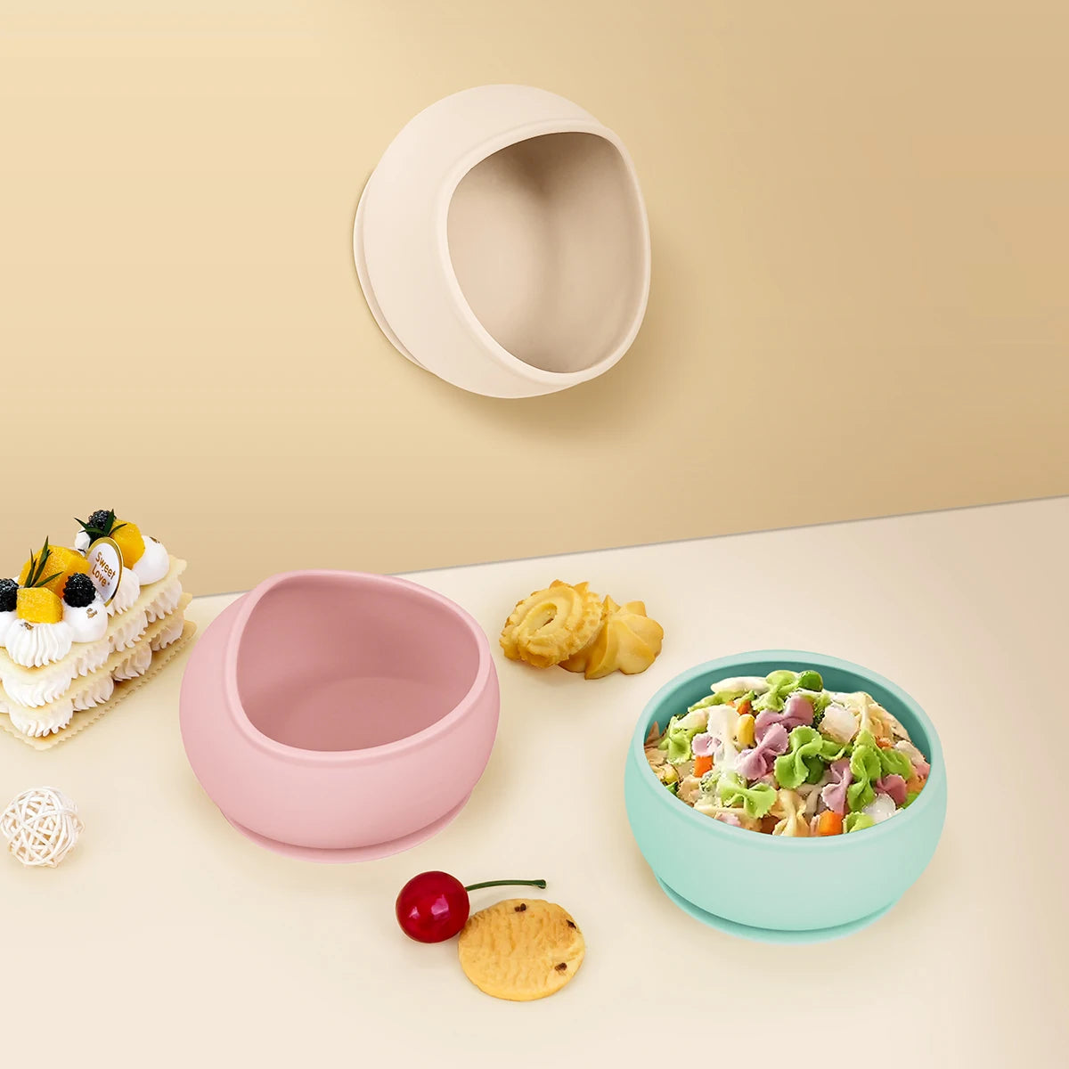 Two bowls, one pink and one blue, on a table with snacks and a cake.