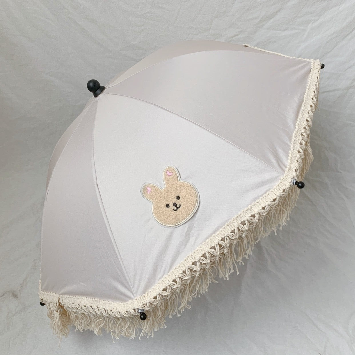 White umbrella with a teddy bear design and lace trim on a white background