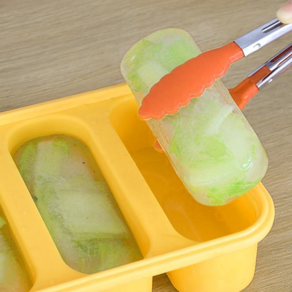 Yellow popsicle mold with green popsicles being removed using orange tongs on a wooden surface.