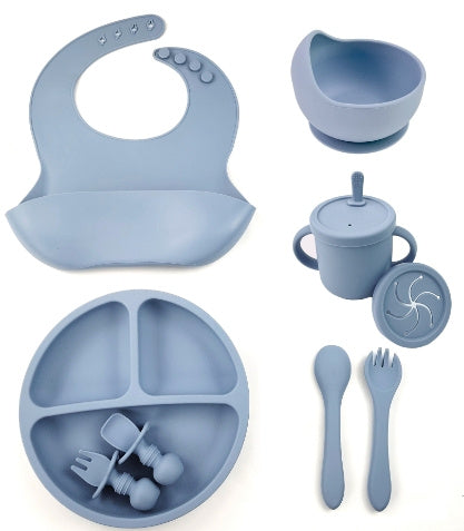 Blue silicone baby feeding set including bib, bowl, cup, spoon, fork, and plate on a white background