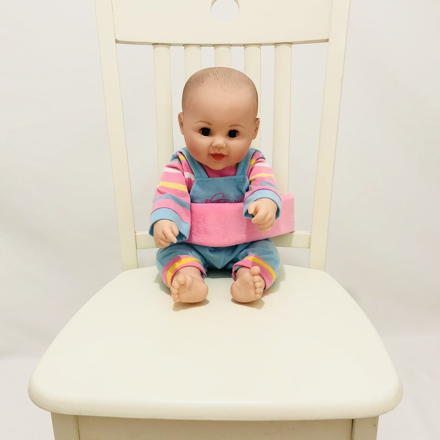 Baby doll sitting on a white chair wearing a colorful outfit with a pink seat.