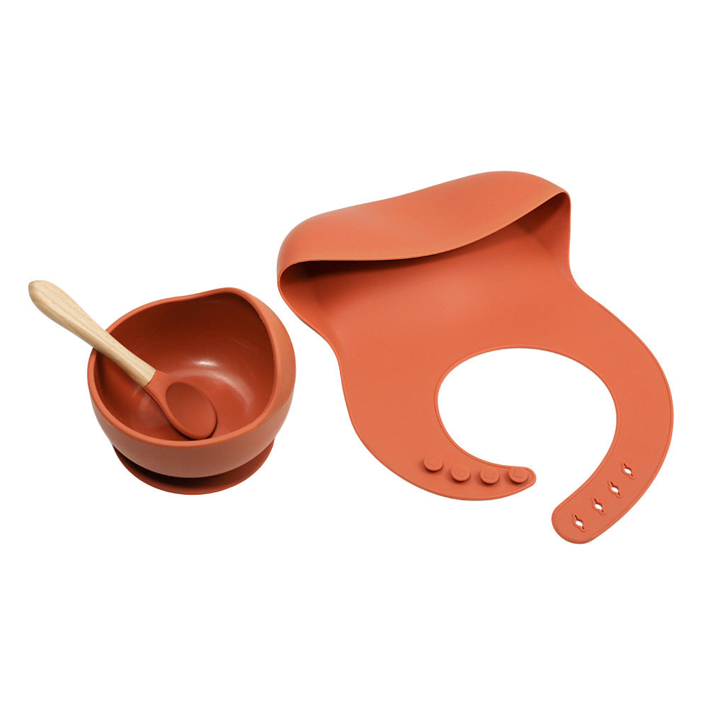 Orange baby bowl, spoon, and bib set on a white background