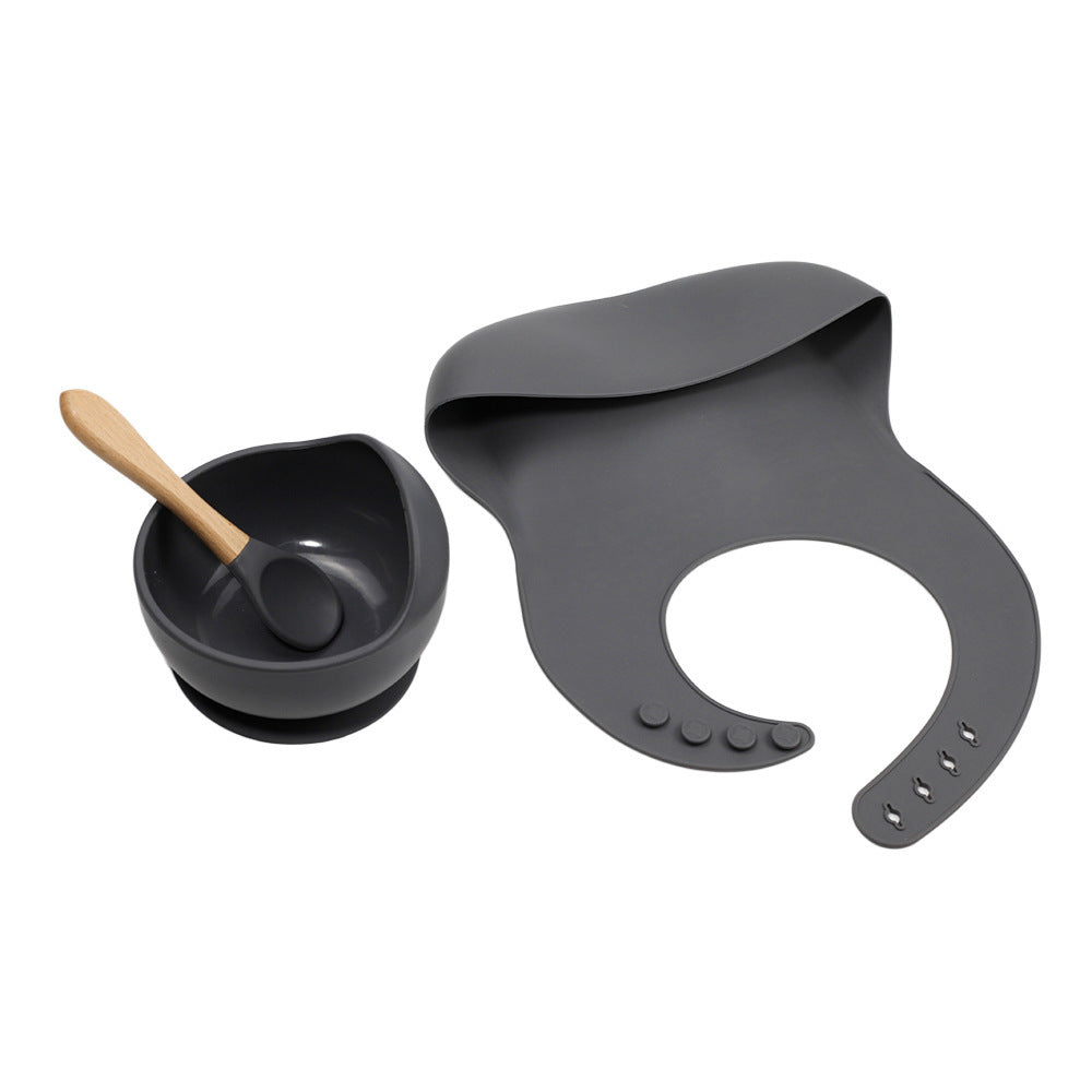 Gray silicone bib, bowl with spoon, and black cup on a white background