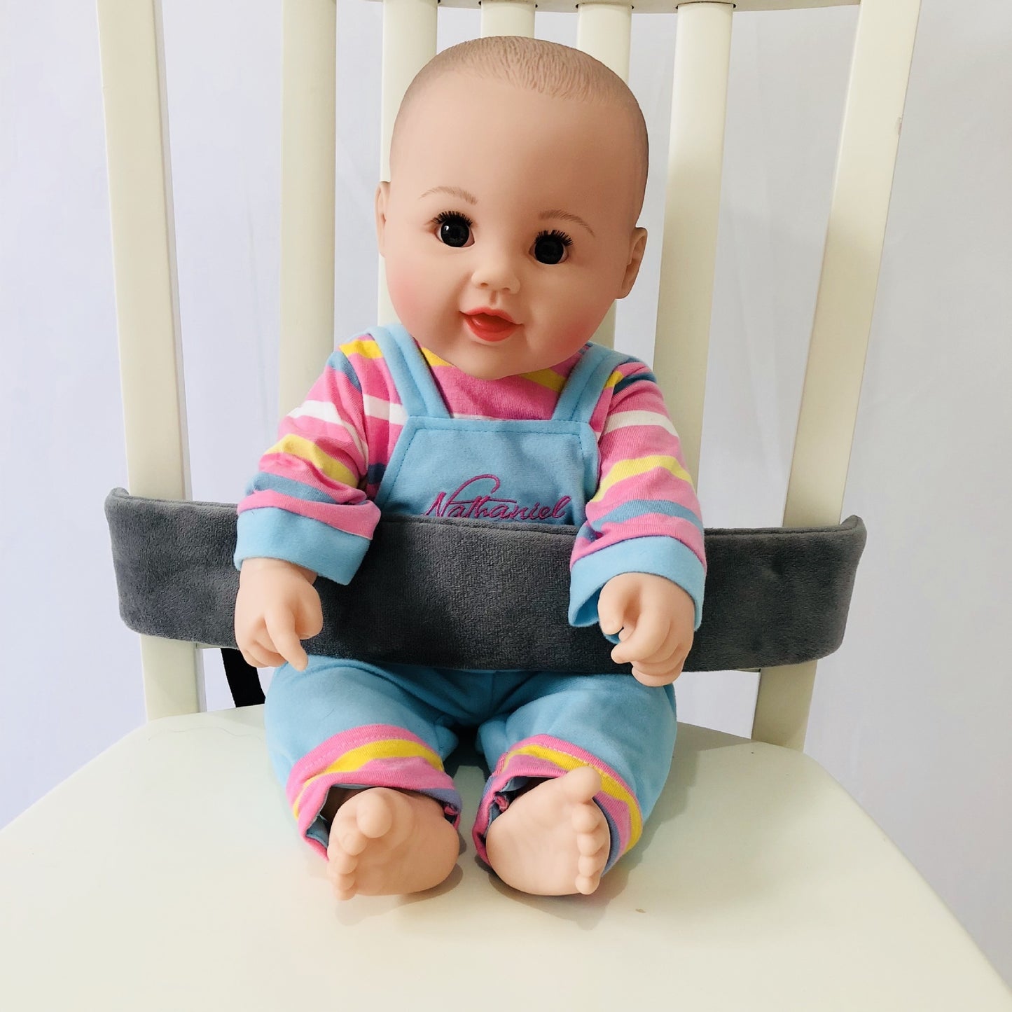 Baby doll wearing a colorful outfit sitting on a chair with a cushion.