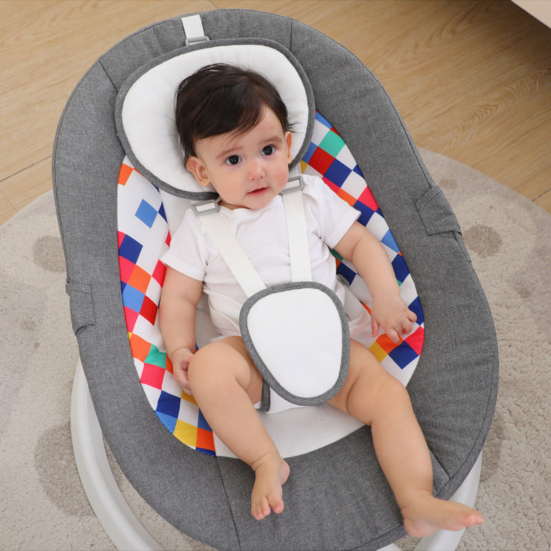 Baby sitting in a gray baby bouncer with colorful diamond pattern on a wooden floor.